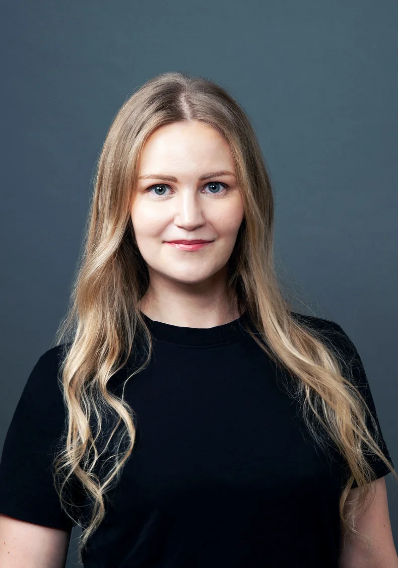 Teresa Koskinen, transition coach, smiling in a black top against a grey backdrop